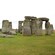 People explore the grass fields behind the monument at Stonehenge